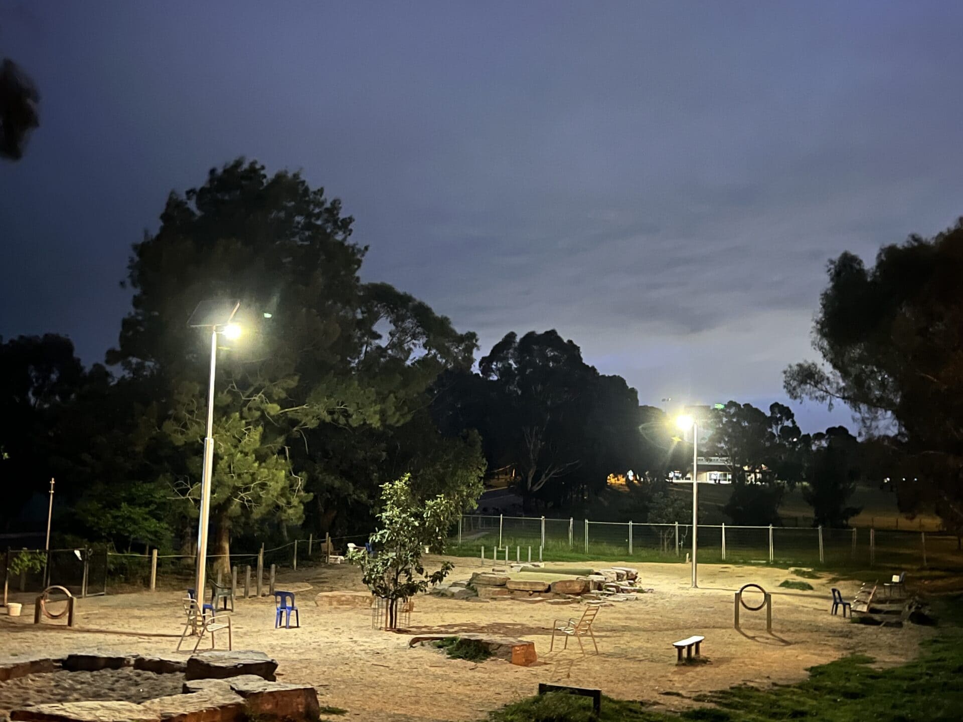 A dimly lit park with benches, playground equipment, and trees is visible at dusk.